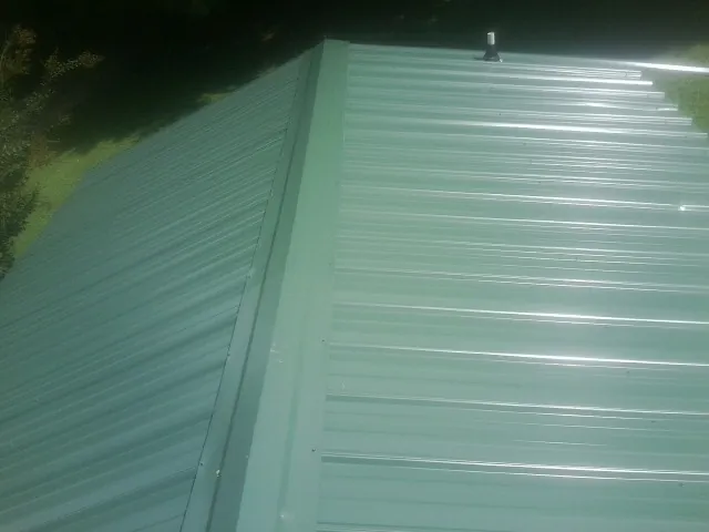 New green metal panels meeting at the ridge of a roof — Flat Roof Repair work by our crew in Alton